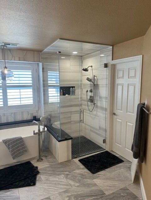 Bright bathroom with glass shower, black accents, bench, window seat, and gray chevron floor tile.