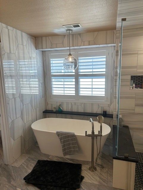 Modern bathroom with freestanding tub, glass shower, tiled walls, and a window above the sink
