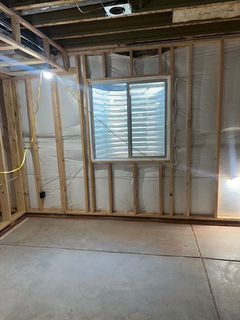 Unfinished room with exposed wall studs, small window, and concrete floor under renovation.