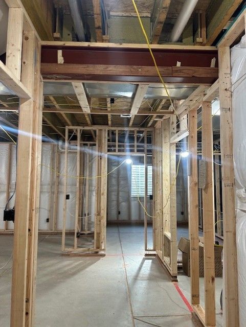 Framed interior of a house under construction with exposed wood studs and ceiling joists.