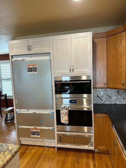 Kitchen with a stainless steel refrigerator and built-in oven wall unit between wood cabinets.