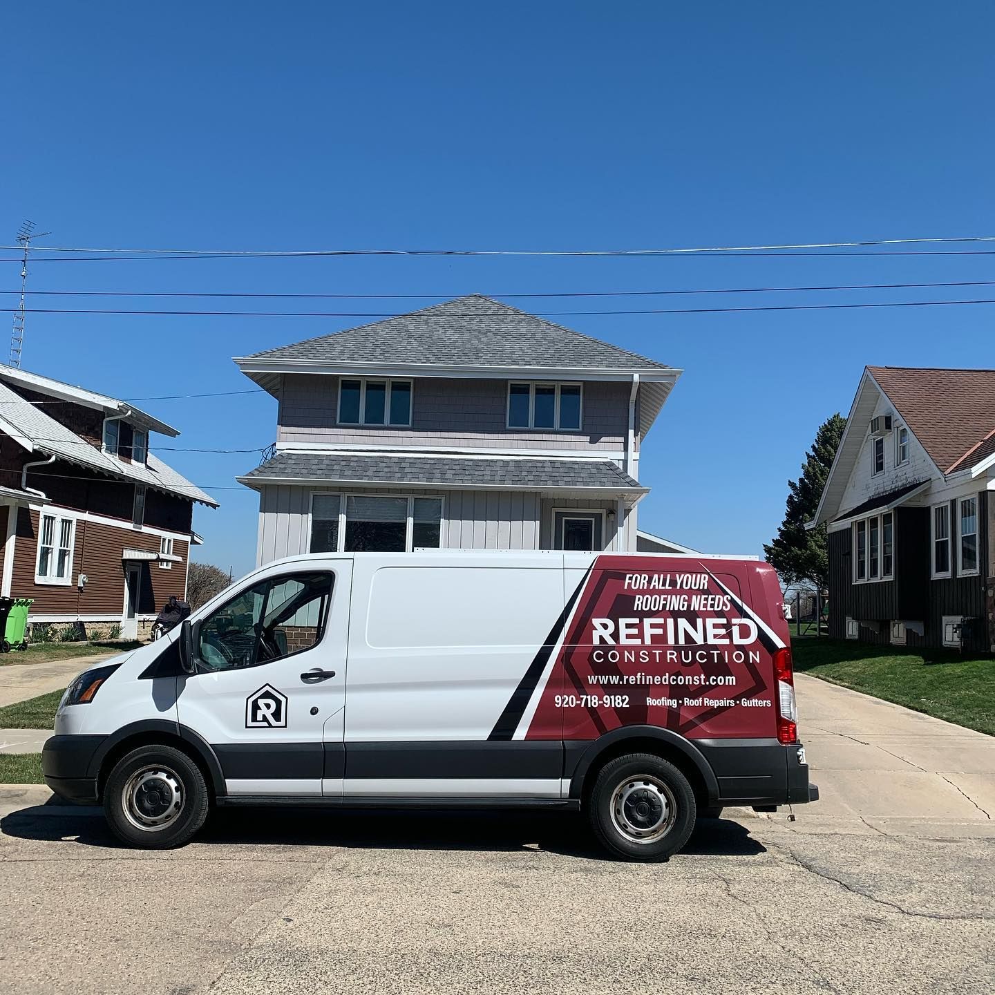 A white van is parked on the side of the road in front of a house.