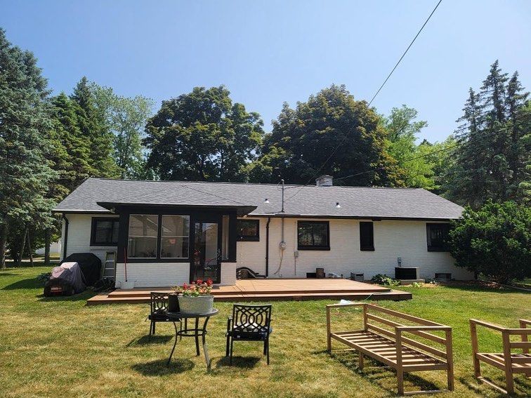 A white house with a black roof sits in the middle of a lush green field.