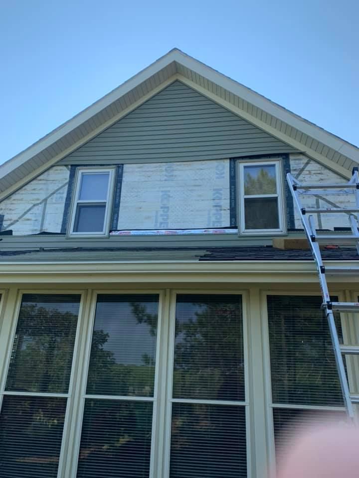 A person is standing on a ladder on the roof of a house.