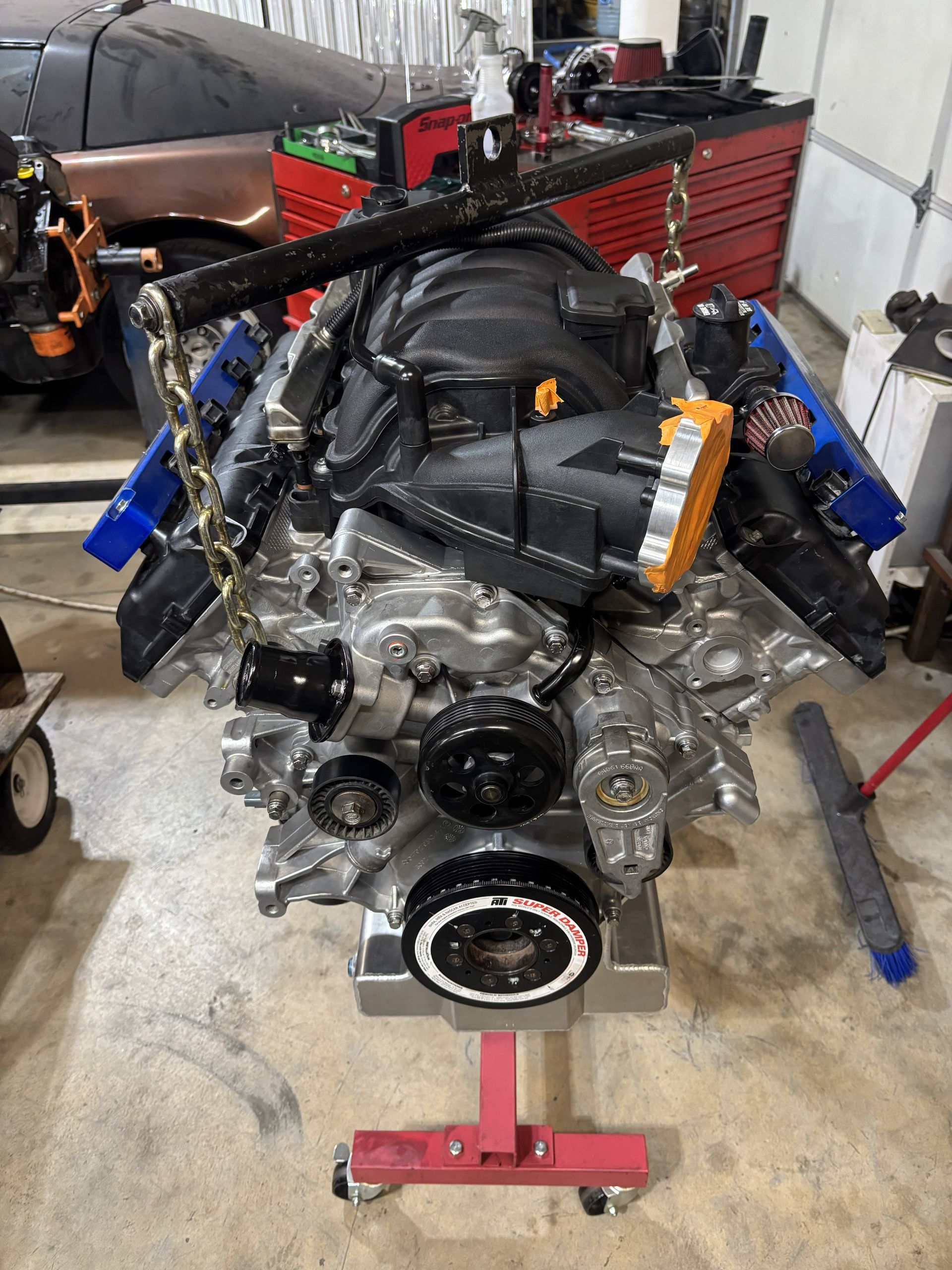 Silver engine on a red engine stand with black and blue components inside a garage.