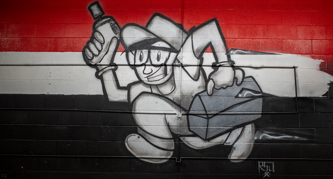 Graffiti of a cartoon character running with a spray can and toolbox against red, white, and black background.