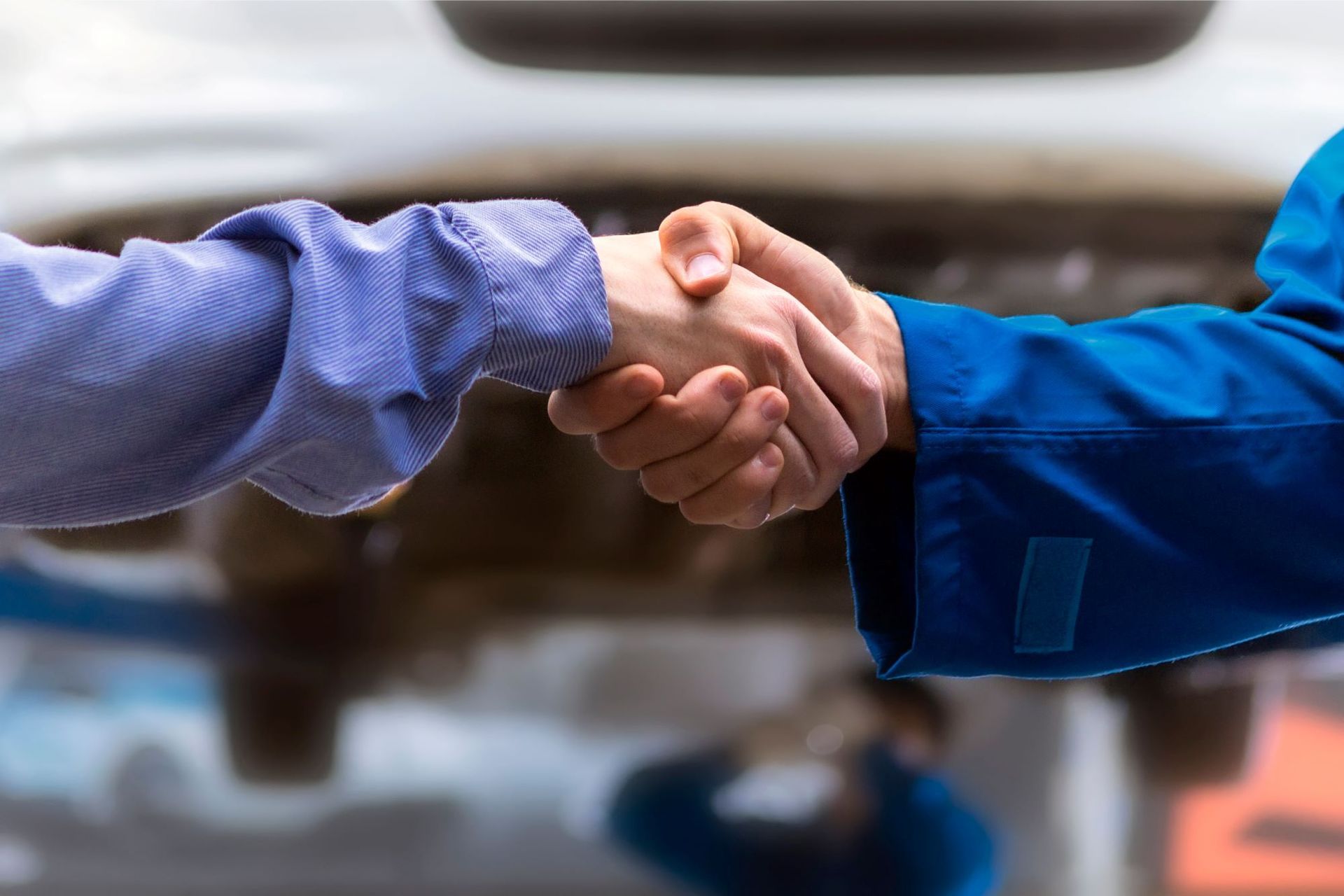 A man and a mechanic are shaking hands in front of a car.