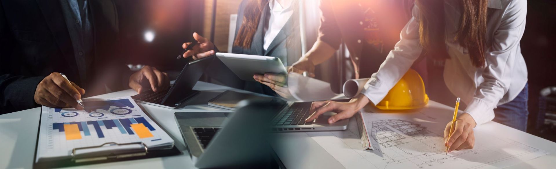 A group of people are sitting at a table looking at a laptop and a tablet.