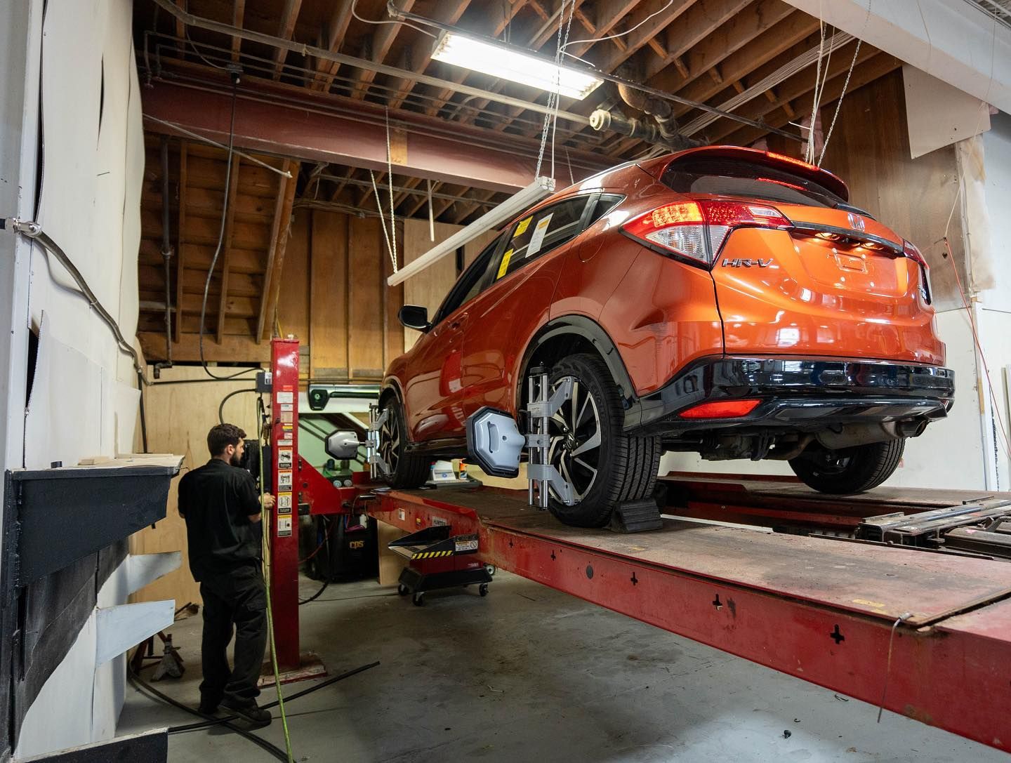 Orange SUV on a lift in a garage, being worked on by a mechanic. | JR Car Care Inc