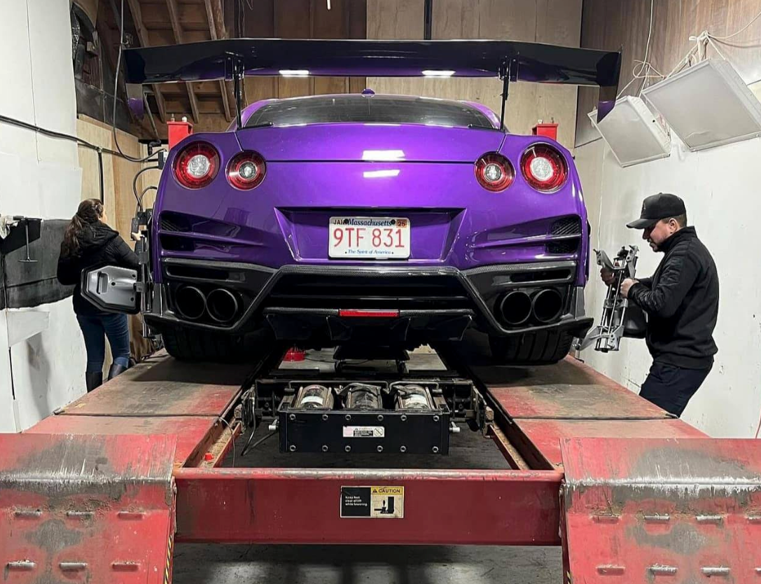 Purple Nissan GT-R on a lift in a garage, two people working on it. | JR Car Care Inc