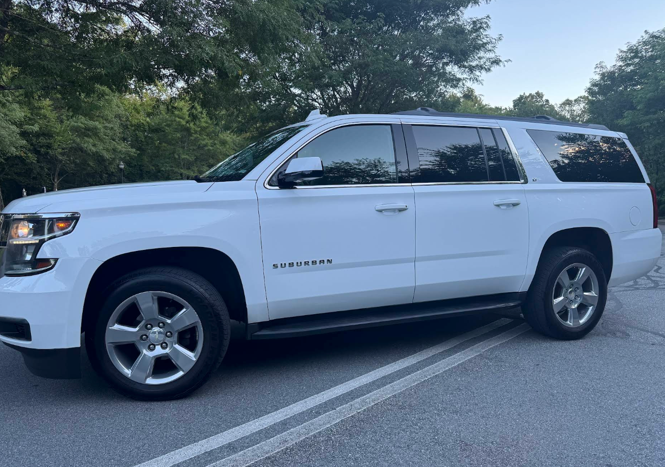 White Chevrolet Suburban parked on a road, trees in the background. | JR Car Care Inc