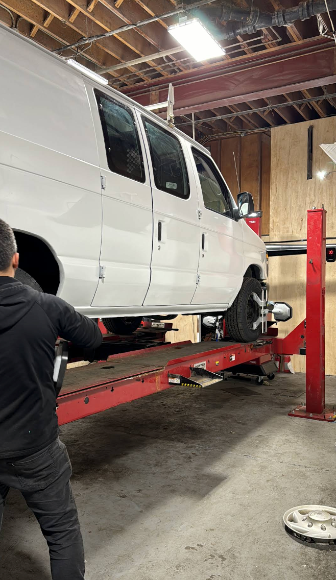 A white van is raised on a red lift in a garage. A person adjusts the lift. | JR Car Care Inc
