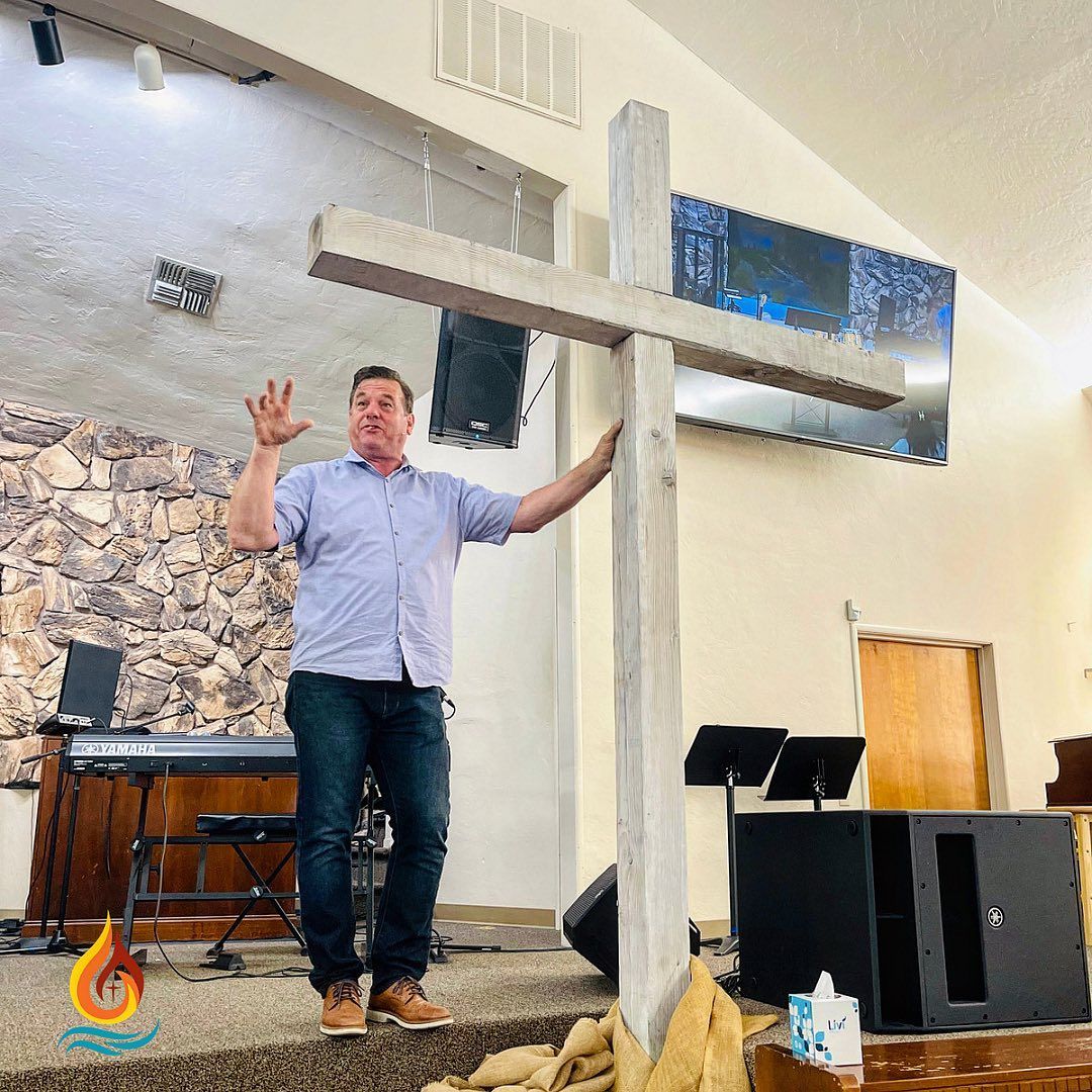 a man is standing in front of a large wooden cross in a church .