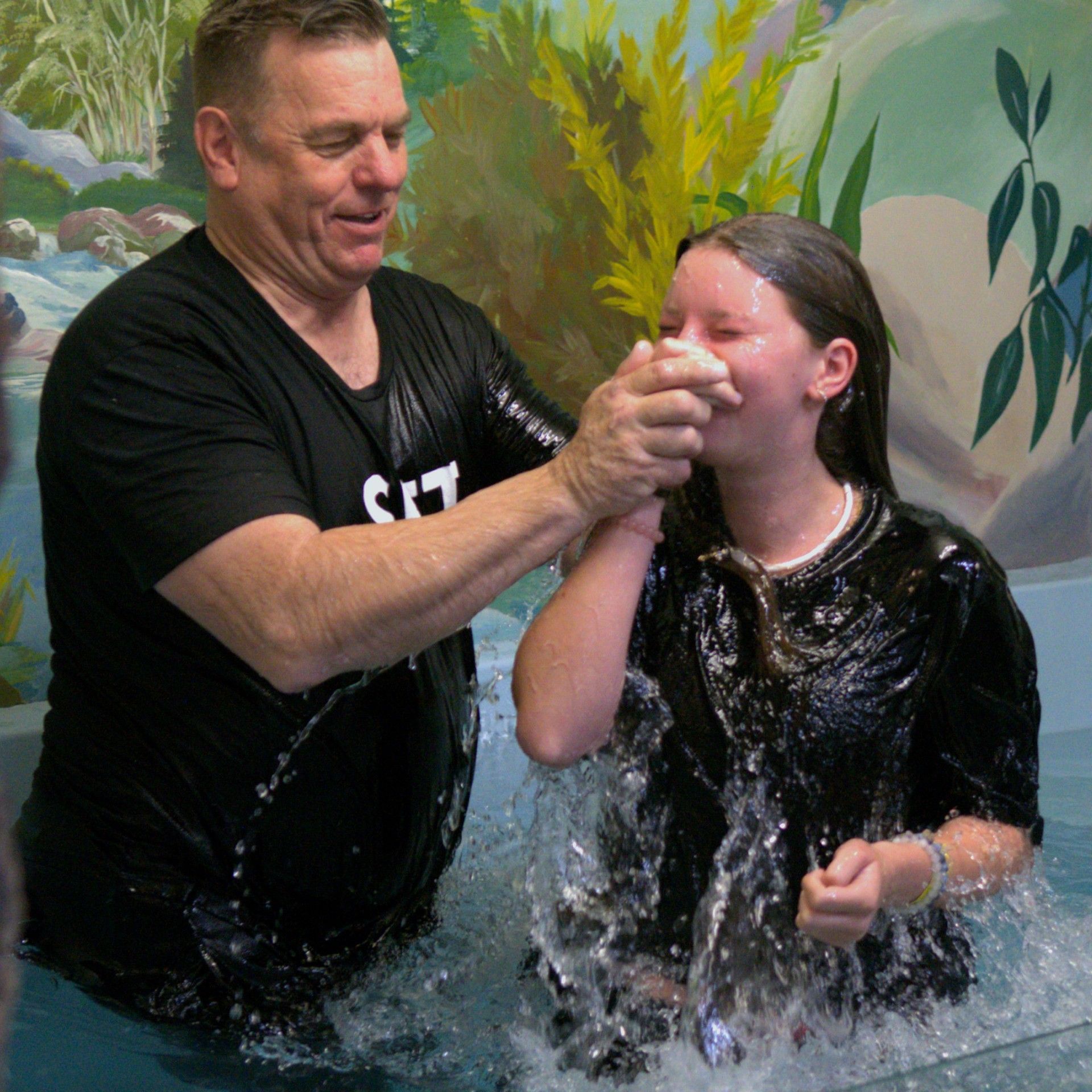 A man in a black shirt is baptising a young girl