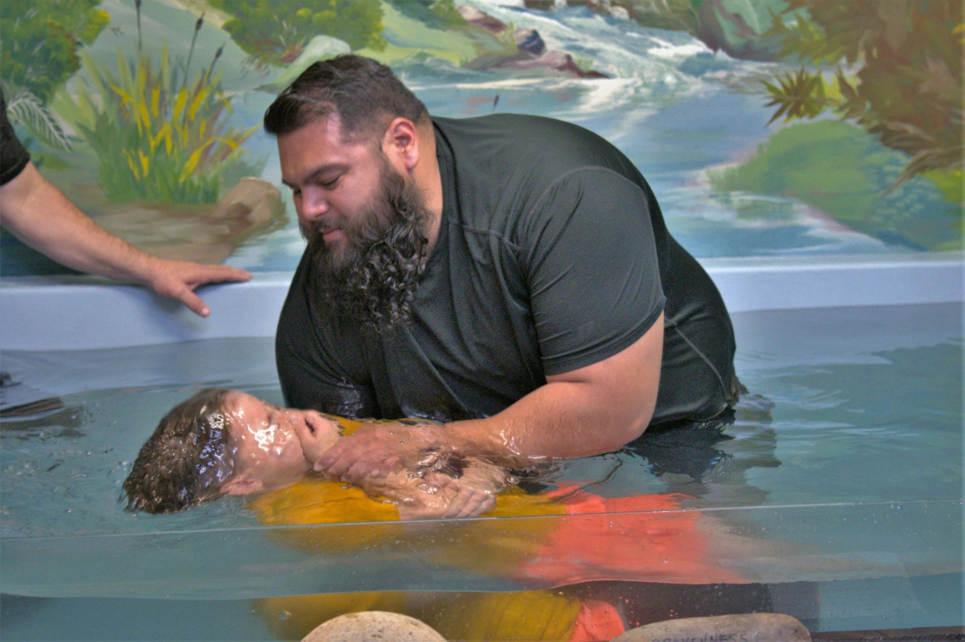 A man is baptizing a child in a pool of water.