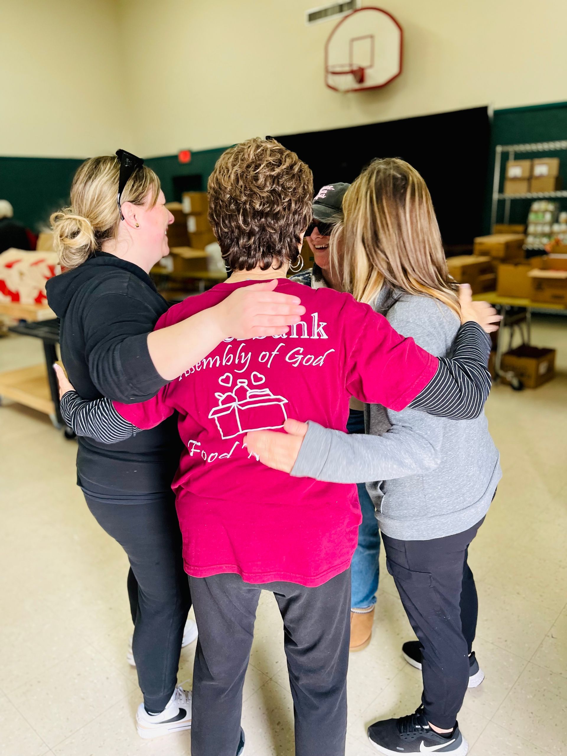 A group of women are hugging each other in a room with a basketball hoop in the background.
