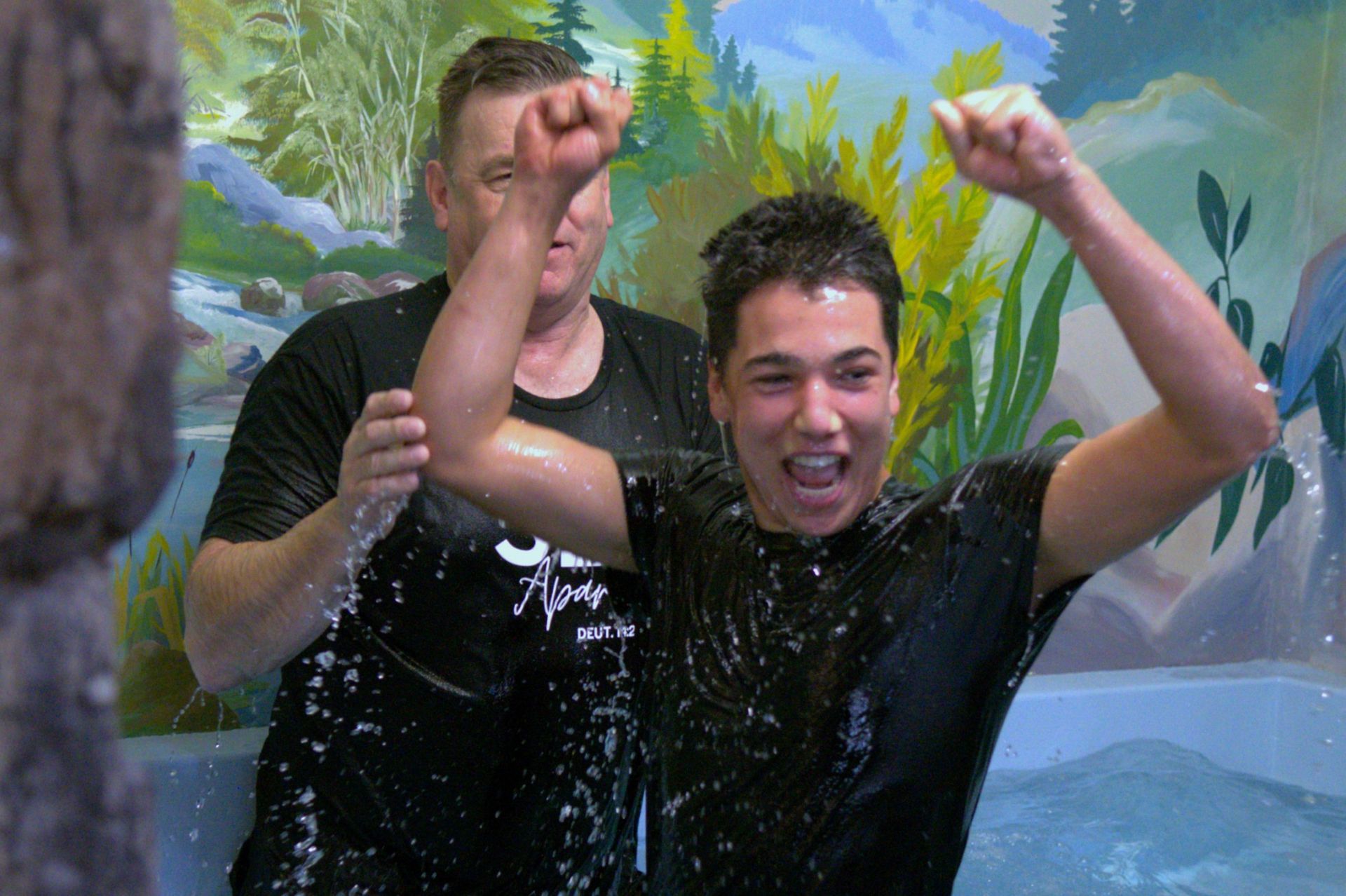 Two men are standing next to each other in a bathtub with their arms in the air.