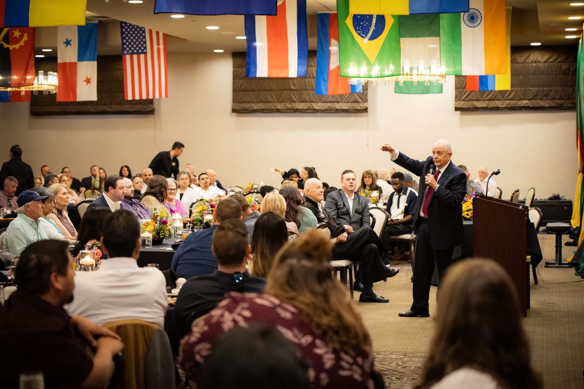 A man is giving a speech at a podium in front of a crowd of people.