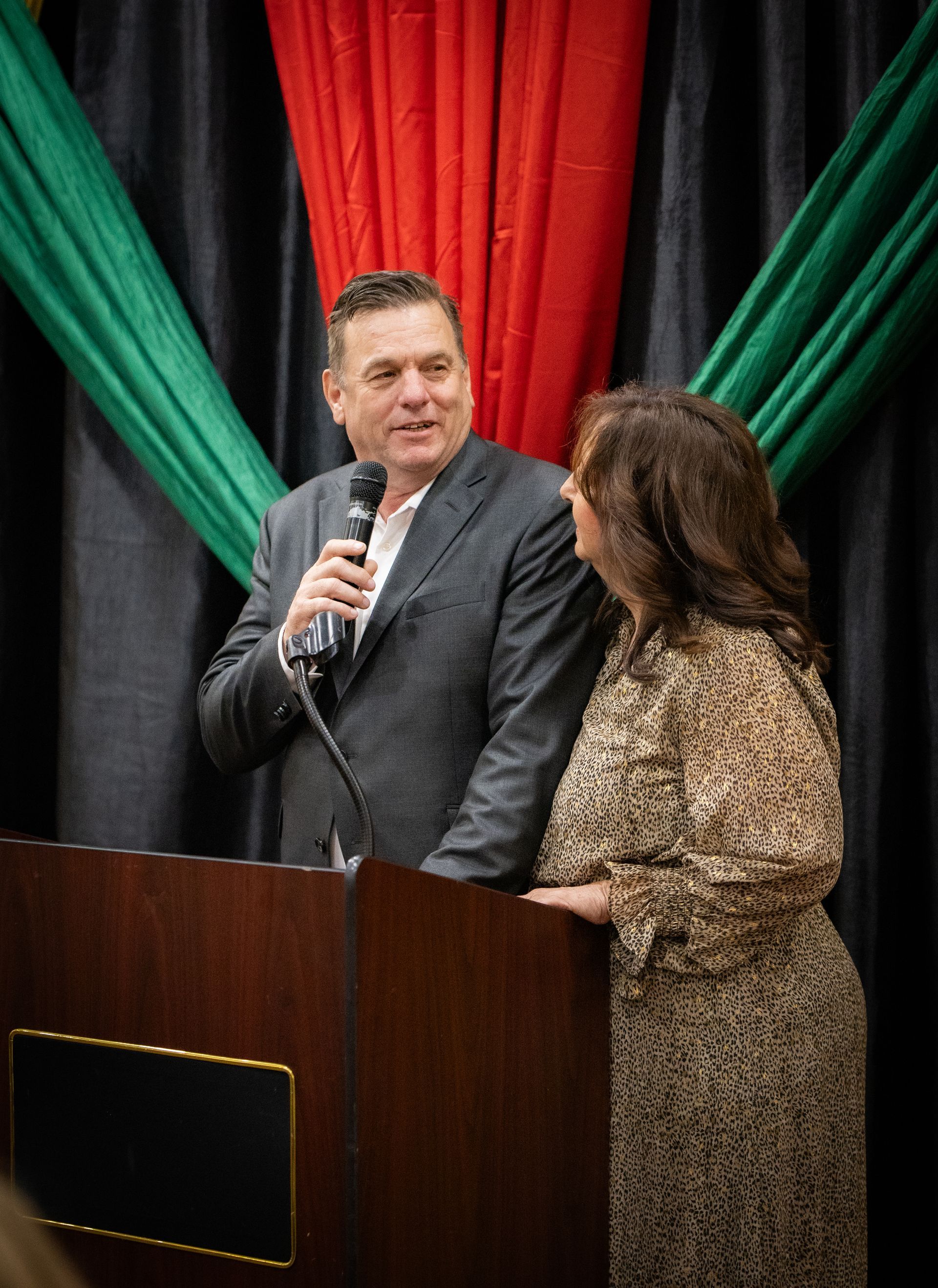 A man and a woman are standing at a podium talking into a microphone.