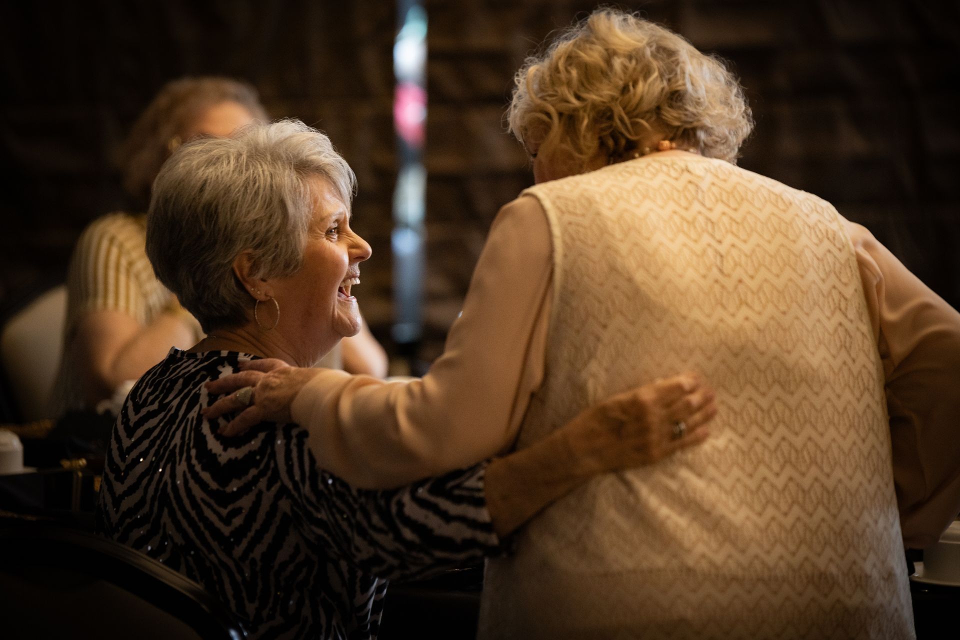 Two older women are hugging each other in a dark room.