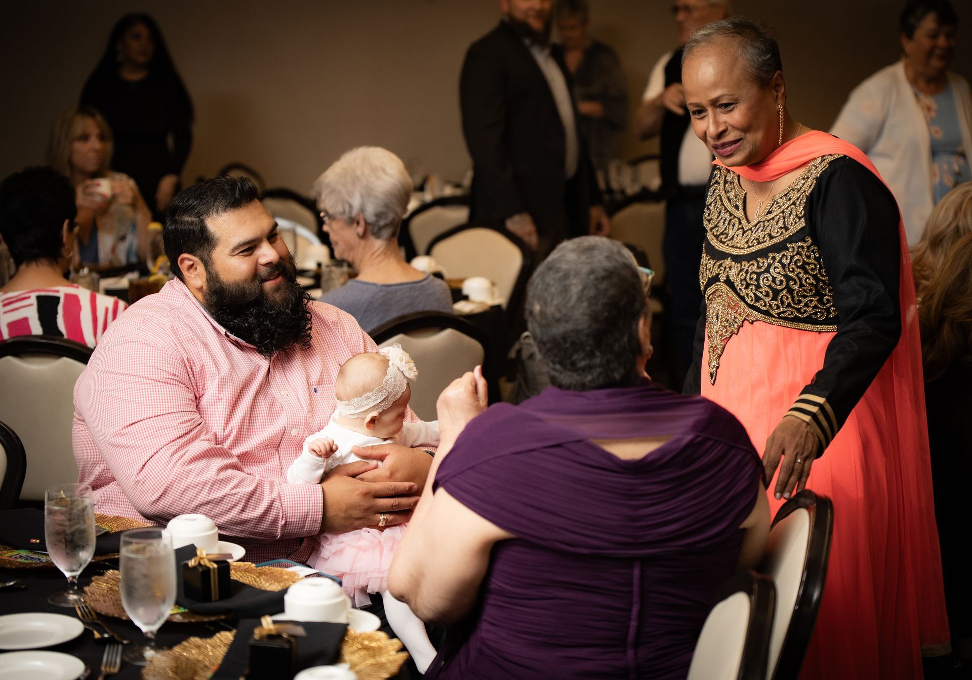 A man is holding a baby while sitting at a table with other people.