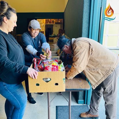 a group of people are standing around a table with a box of food .