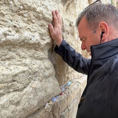 a man wearing ear buds is touching a stone wall .