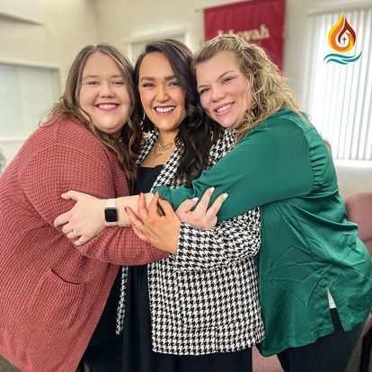 three women are hugging each other in a room .