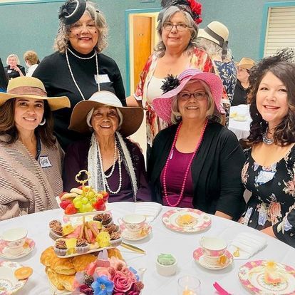 a group of women are sitting at a table wearing hats .