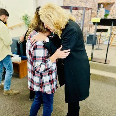 a woman in a plaid shirt is hugging another woman in a black coat .