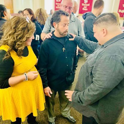 a group of people are standing around a man with a cross on his shirt .