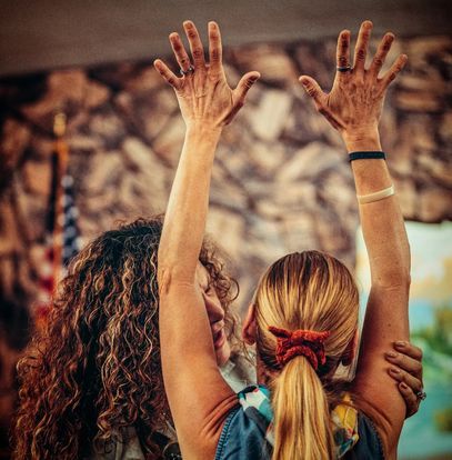 two women are standing next to each other with their hands in the air .