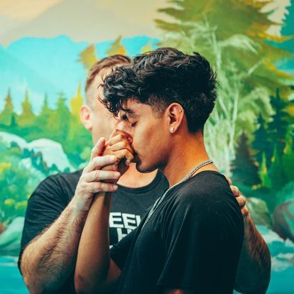 two men are holding hands in front of a painting .