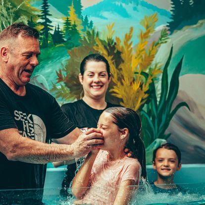 a man is baptizing a little girl in a pool of water .