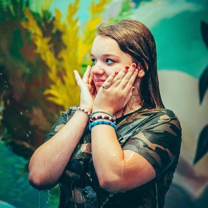 a girl in a camouflage shirt is covering her face with her hands