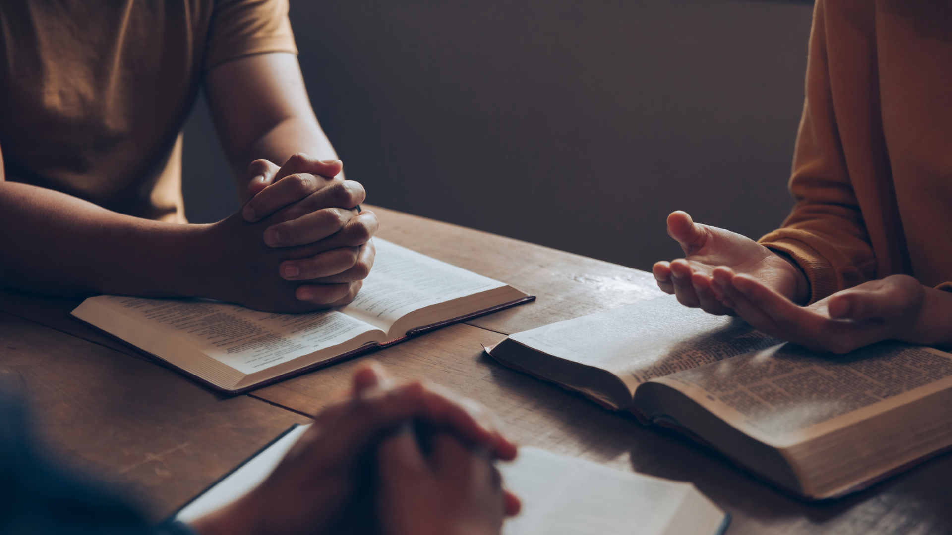 a group of people are sitting at a table with their hands folded in prayer .