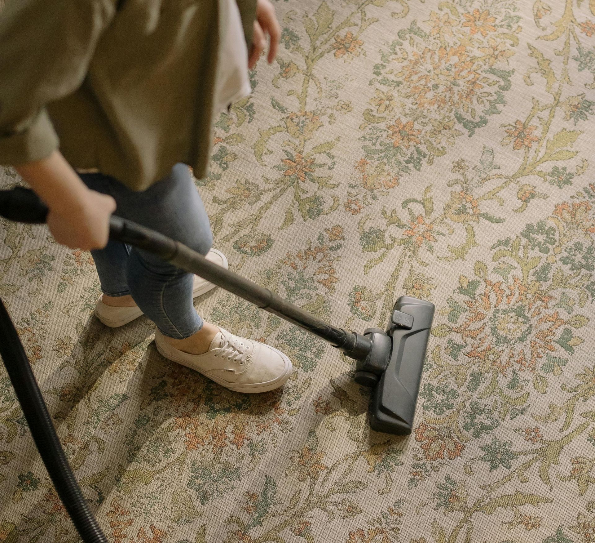 A woman is using a vacuum cleaner to clean a rug.