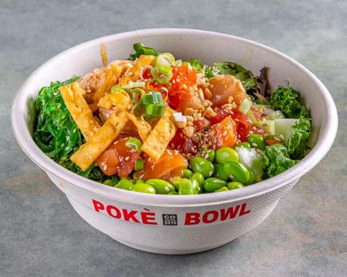 Poke bowl with orange rice, edamame, and greens in a white container on a wooden table