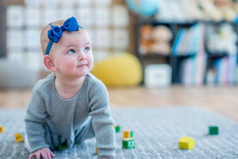 A baby girl with a blue bow on her head is crawling on the floor.