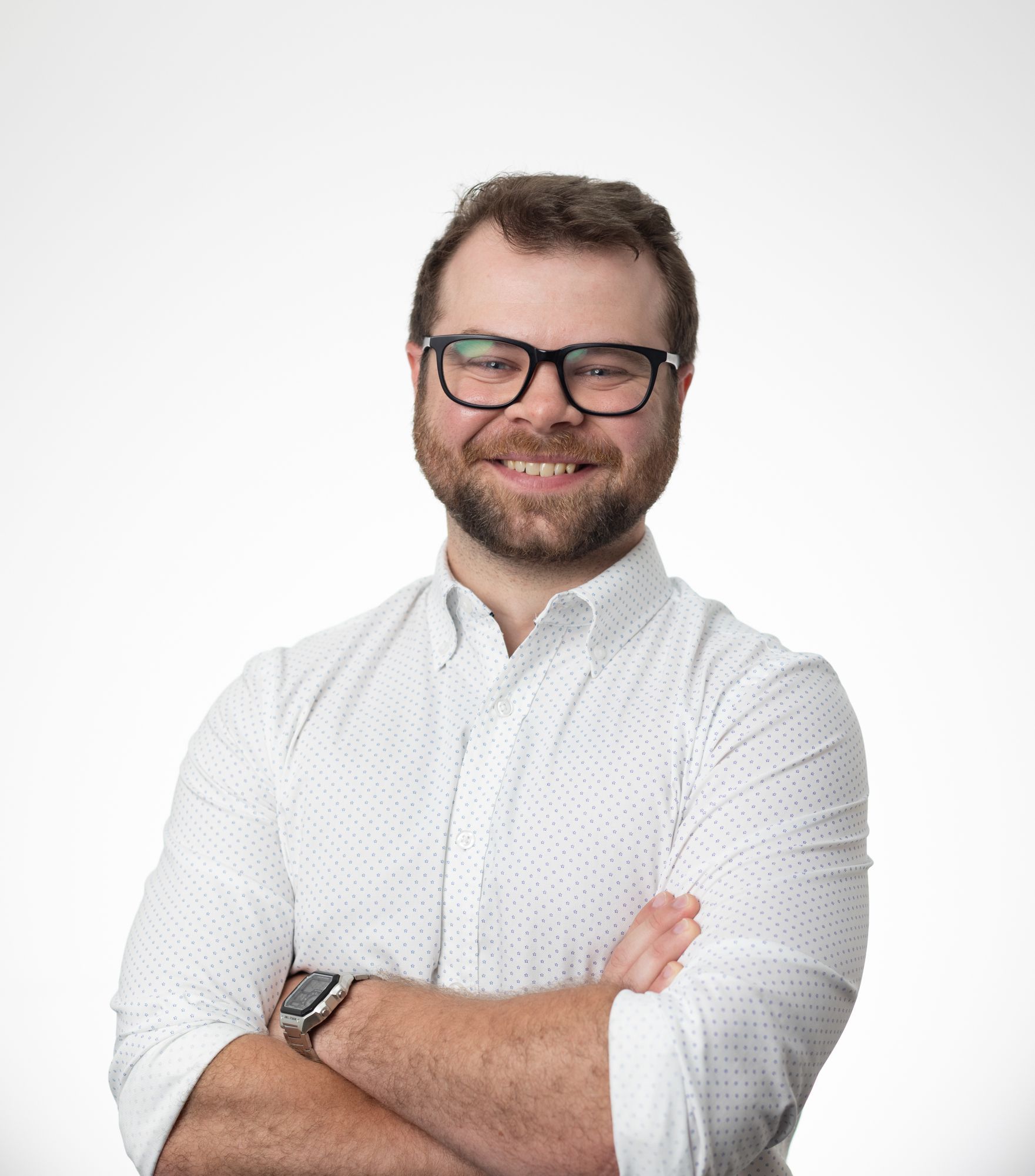 A man wearing glasses and a white shirt is standing with his arms crossed.