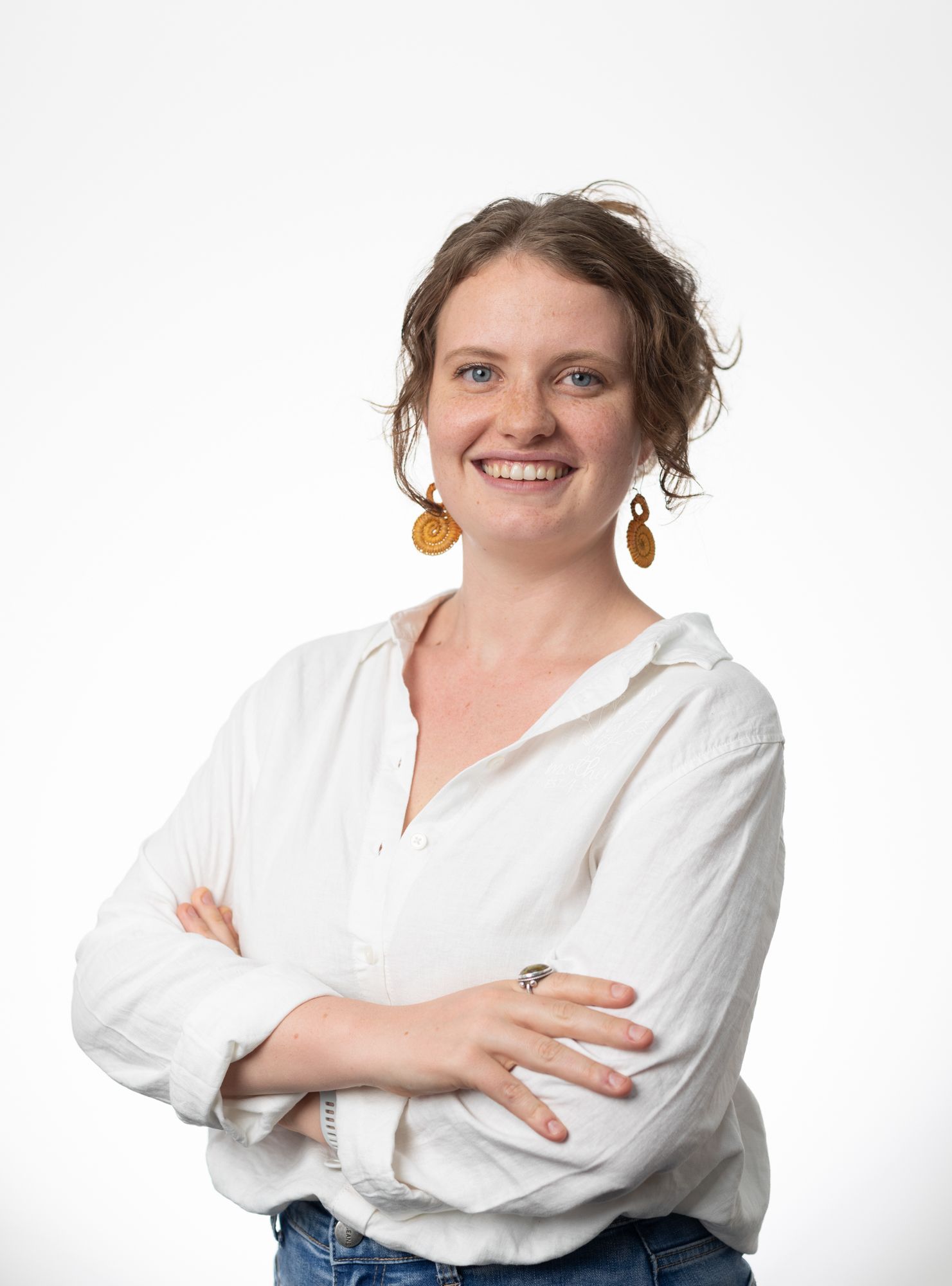A woman in a white shirt and jeans is standing with her arms crossed and smiling.