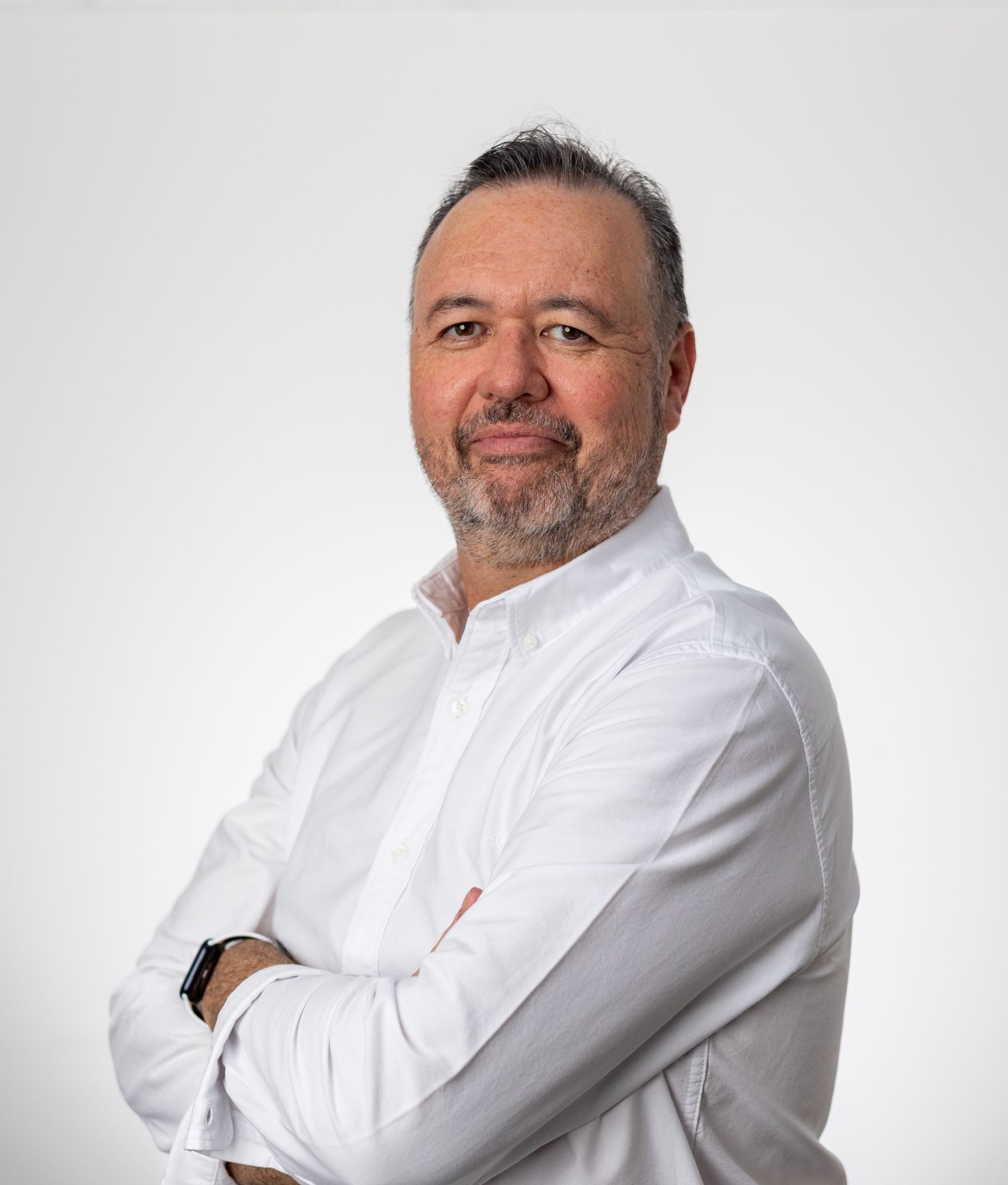 A man with a beard is wearing a white shirt with his arms crossed.