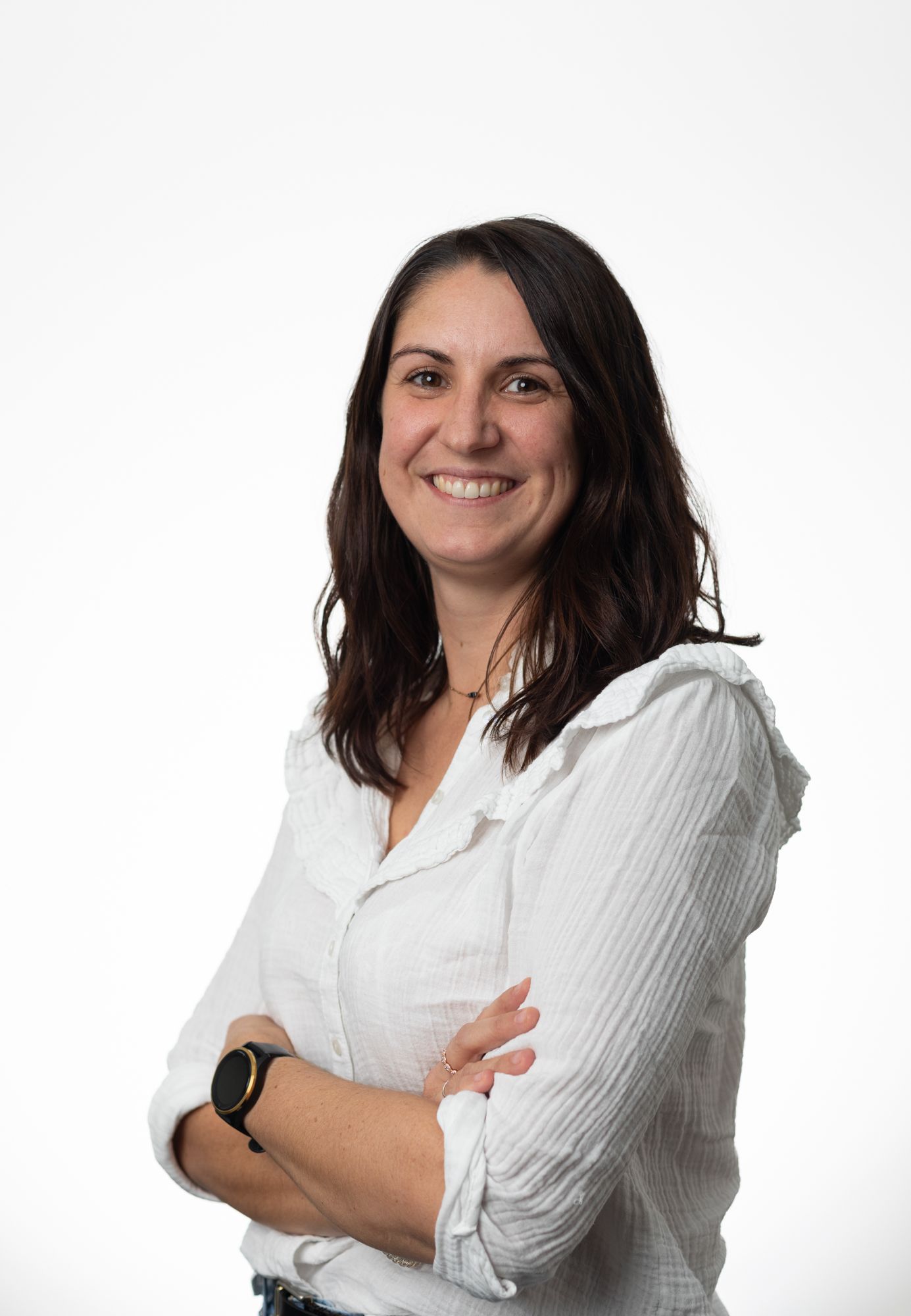 A woman in a white shirt is smiling with her arms crossed.