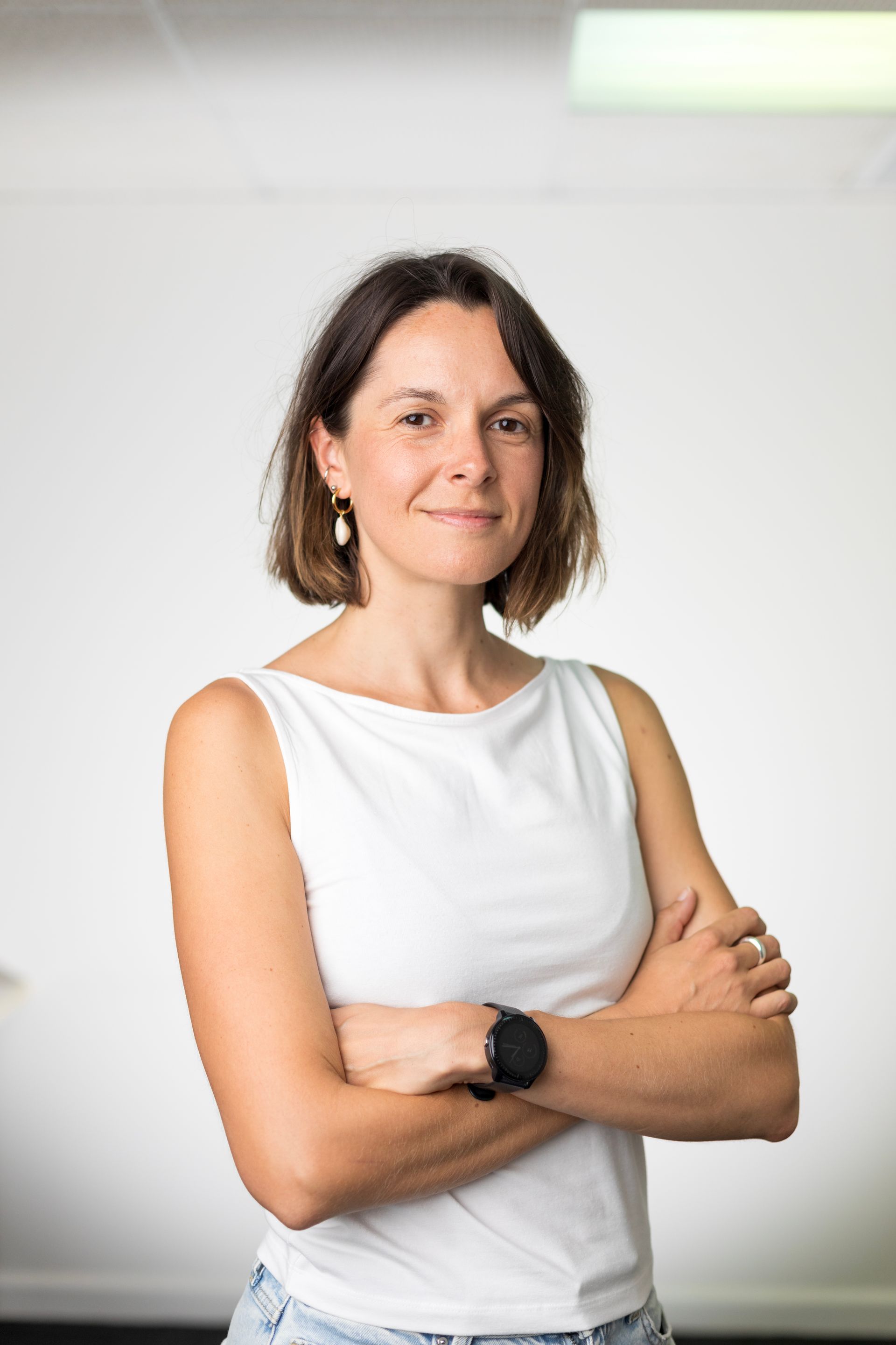 A woman in a white tank top and jeans is standing with her arms crossed.
