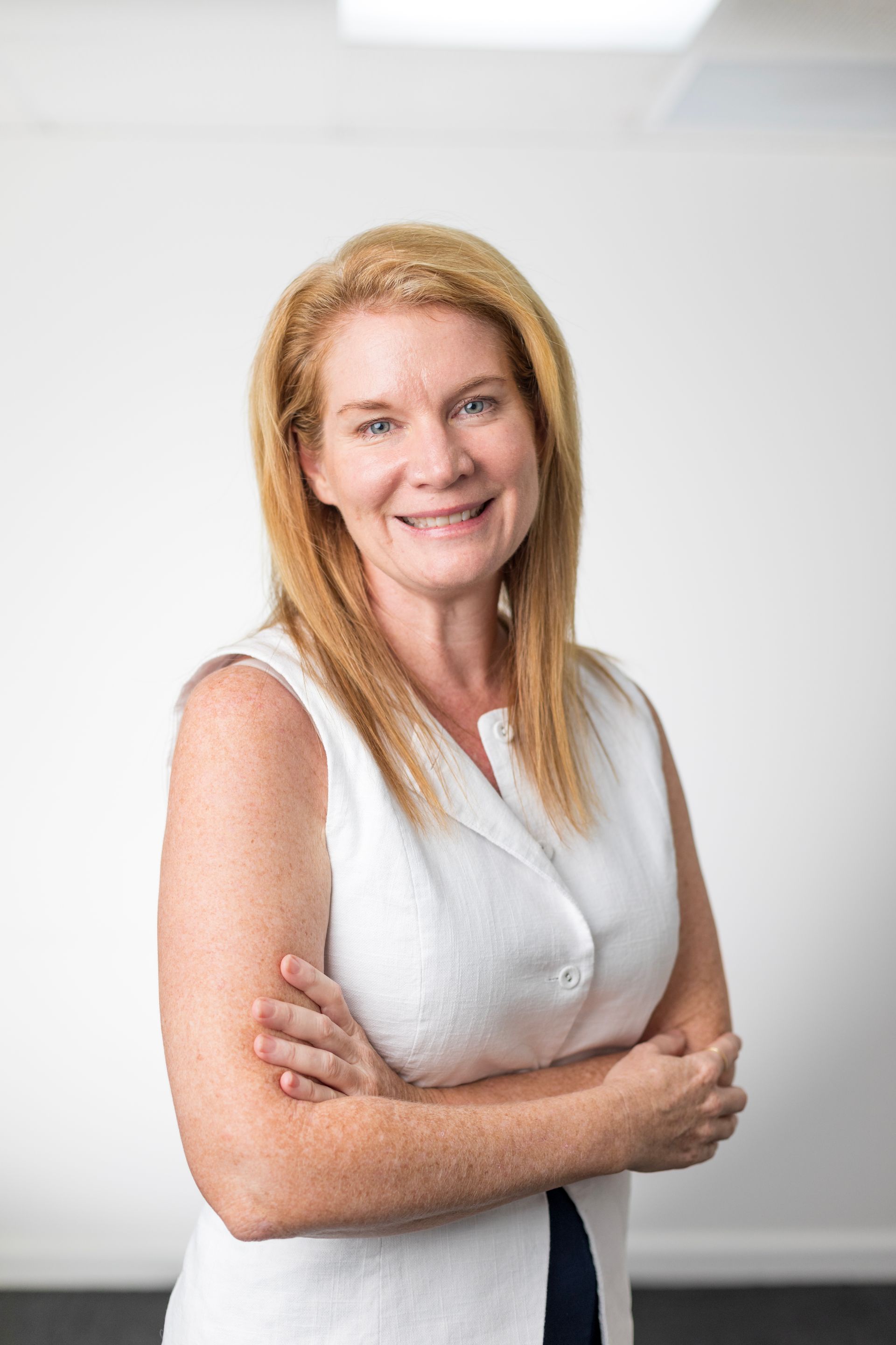 A woman in a white shirt is standing with her arms crossed and smiling.