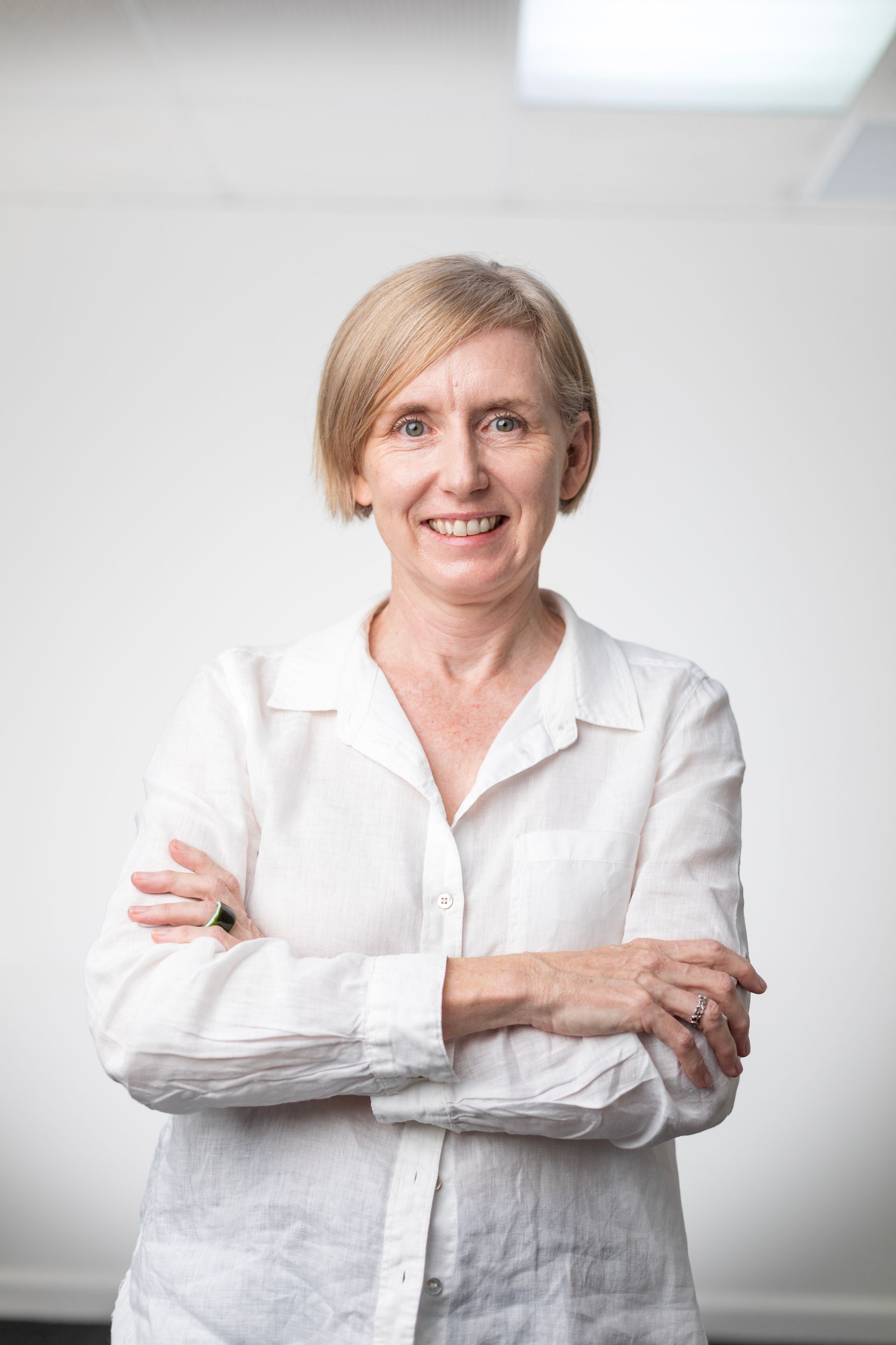 A woman in a white shirt is standing with her arms crossed and smiling.