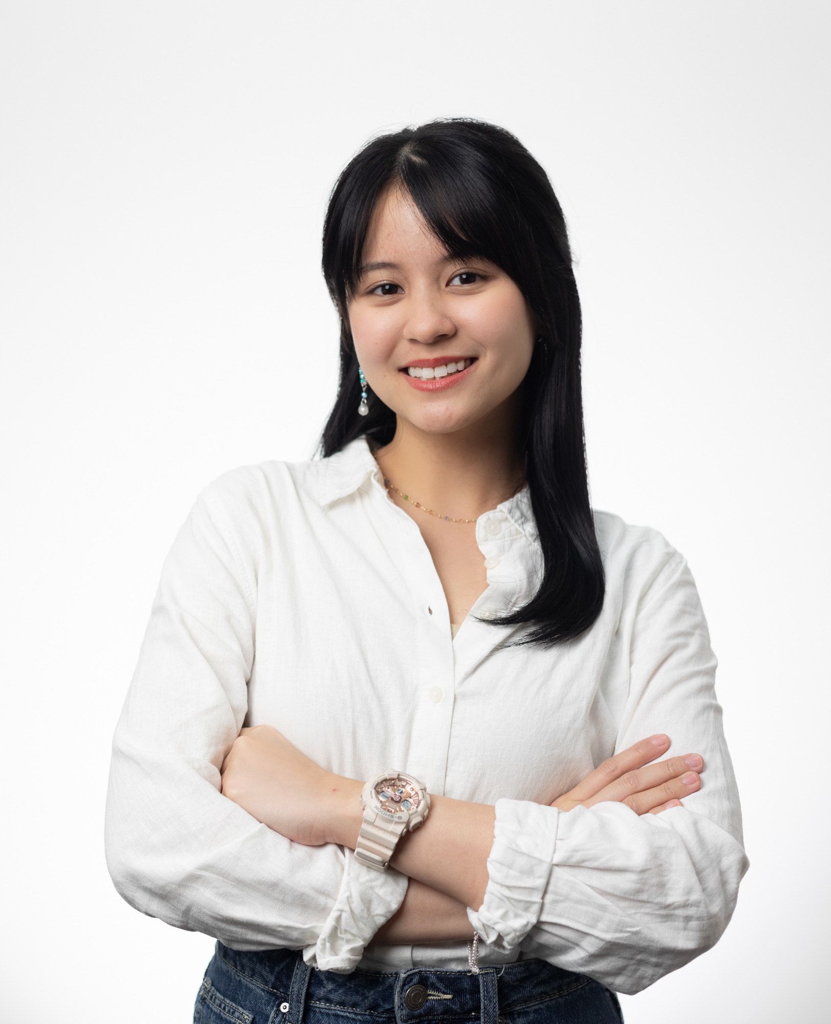 A woman wearing a white shirt and a watch is standing with her arms crossed.