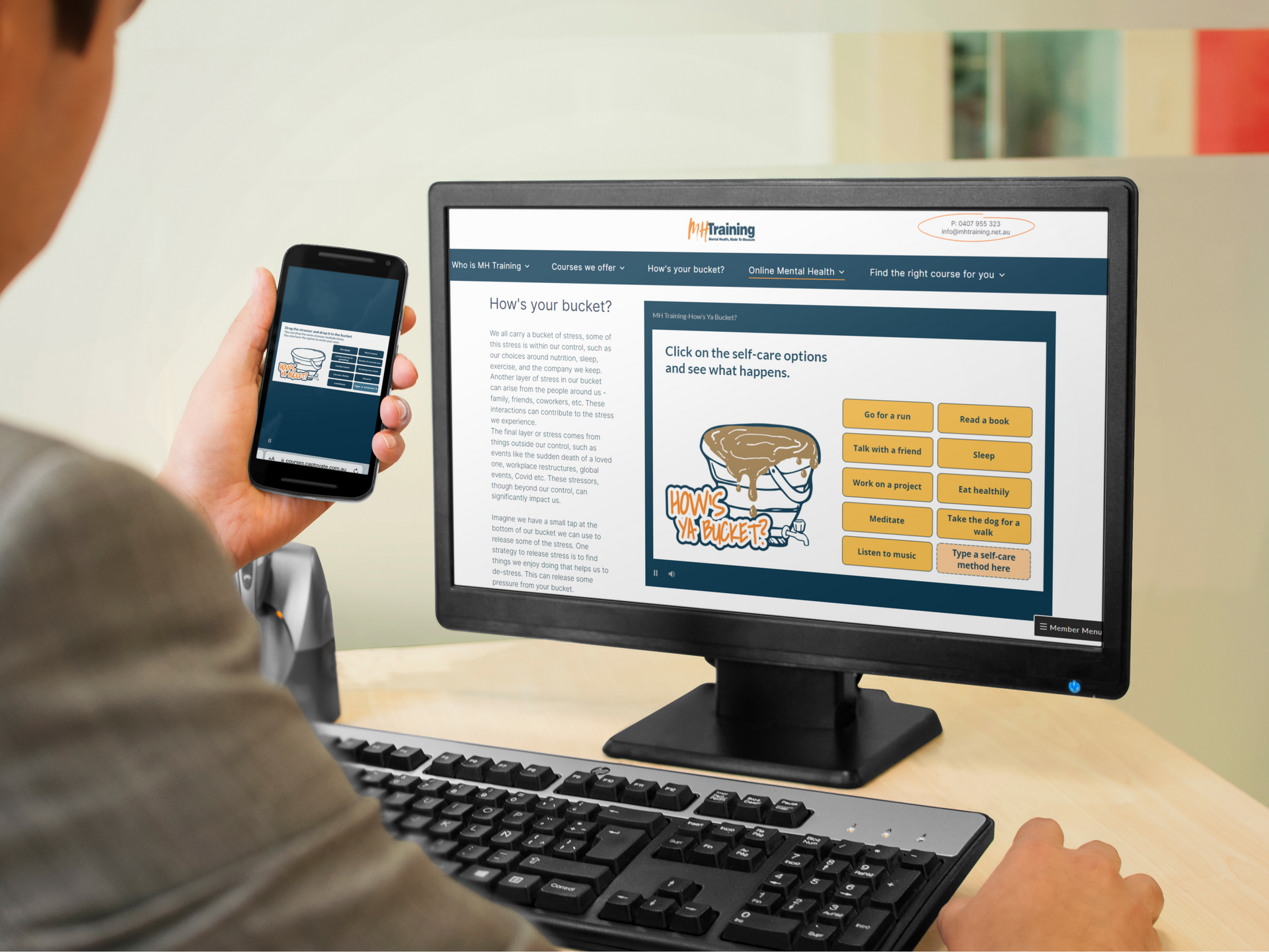 A man is holding a cell phone in front of a computer screen.
