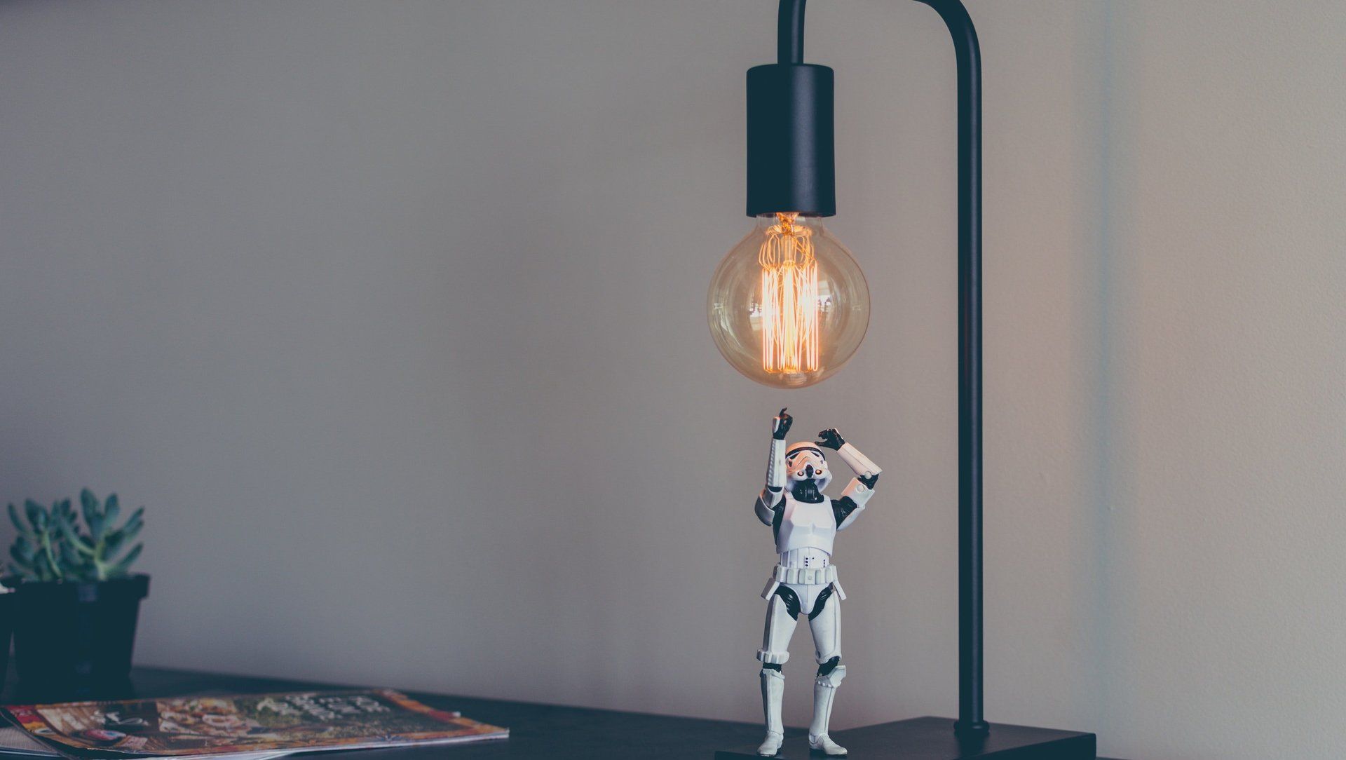 A storm trooper figurine is standing next to a lamp on a table.