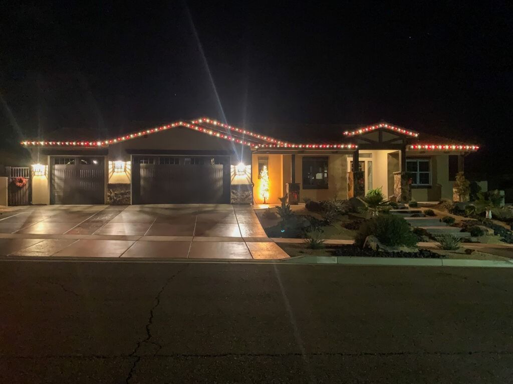 A single-story house at night outlined with glowing orange holiday lights, featuring a garage and a landscaped yard.